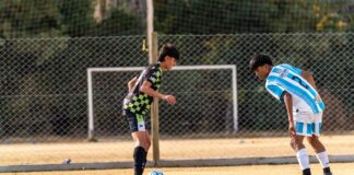 Young athletes engaged in a competitive soccer match outdoors on a sunny day.