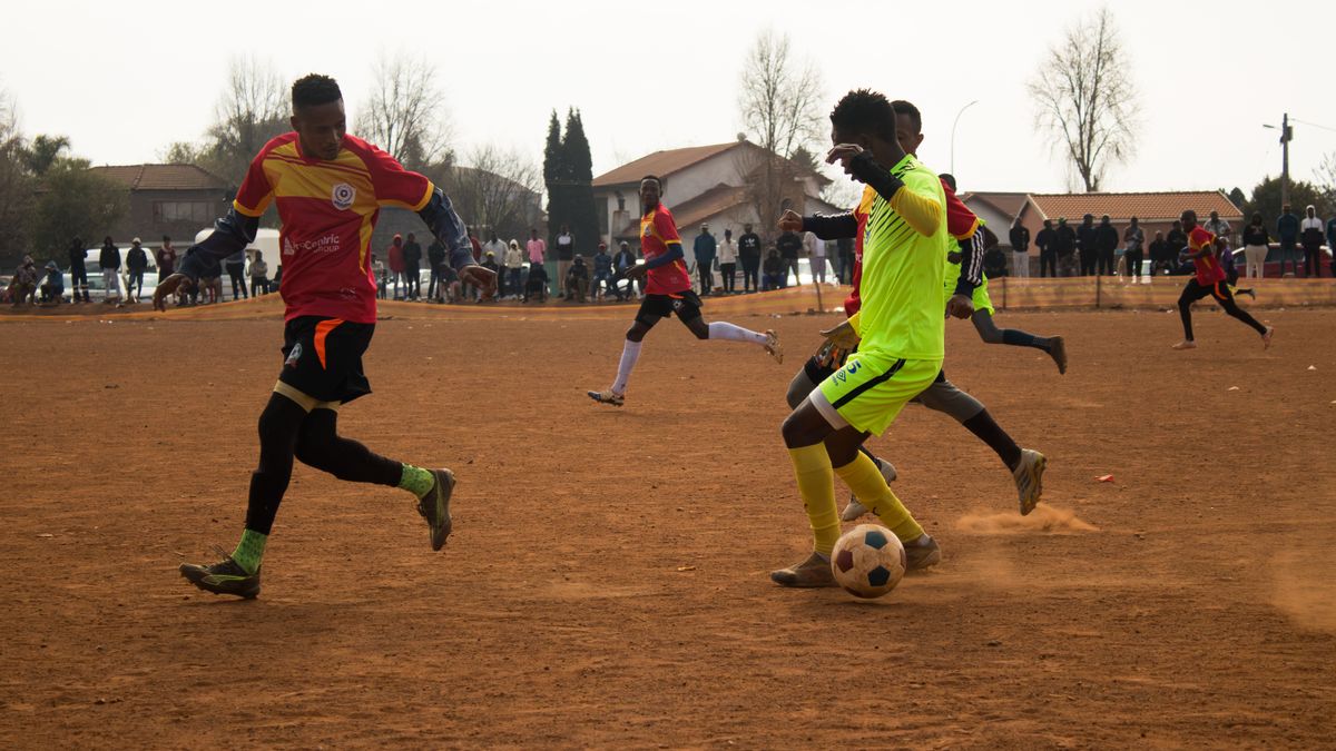 Youth soccer players in action on a dusty field with a lively crowd watching.