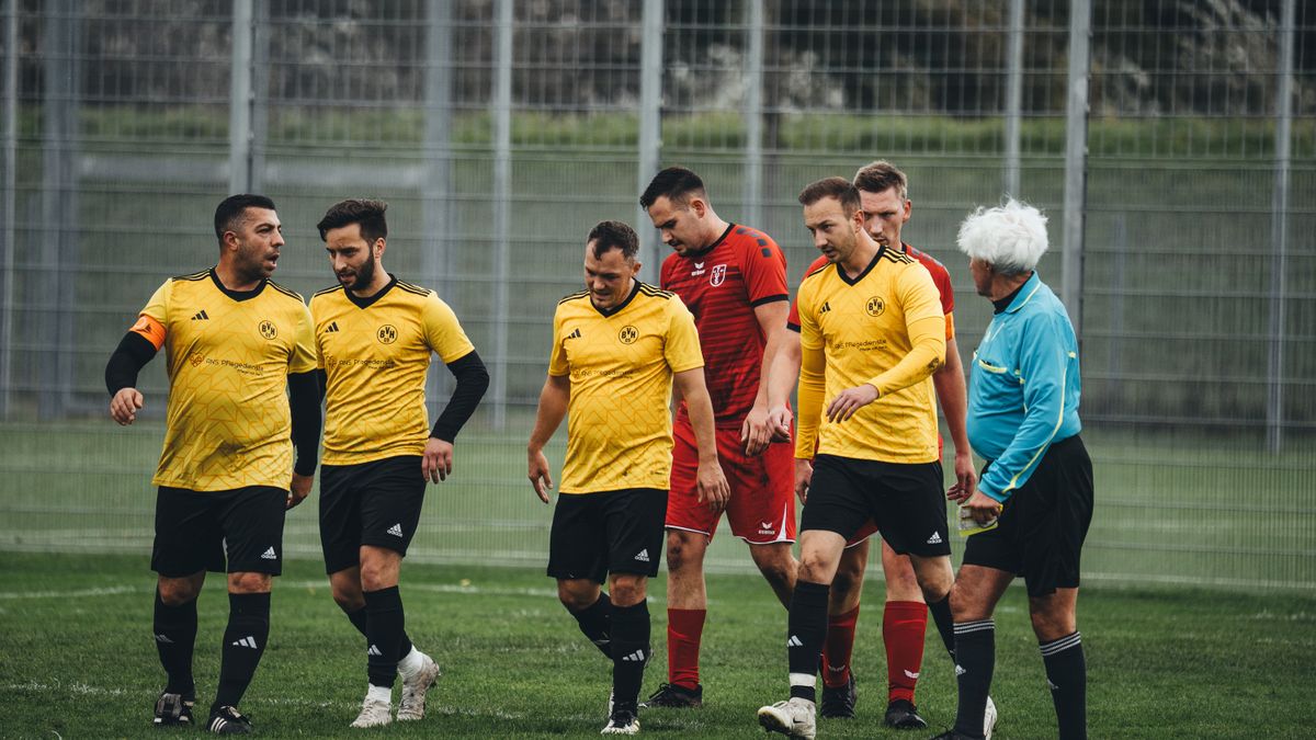 Amateur soccer players in yellow uniforms and referee on the field after a match.