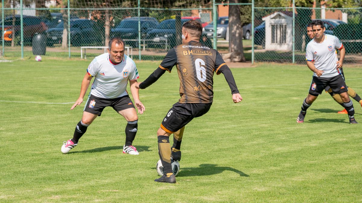Adult men playing a friendly soccer game on a grassy field under clear skies.