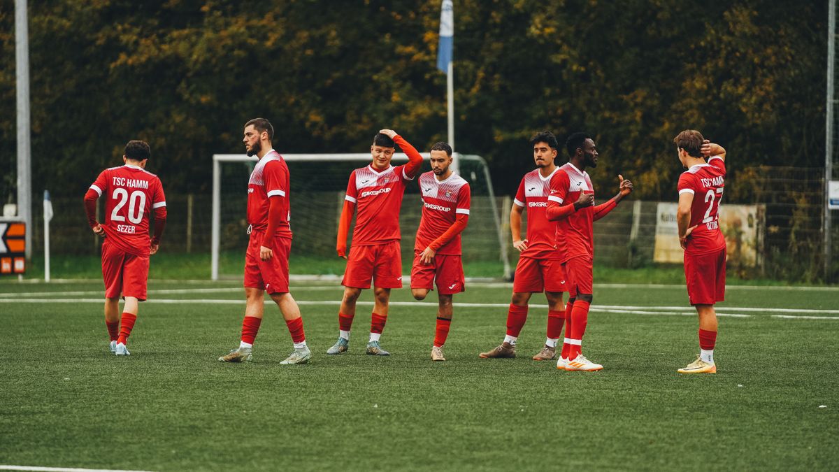 Amateur soccer team in red uniforms gathering on a green field during daytime.