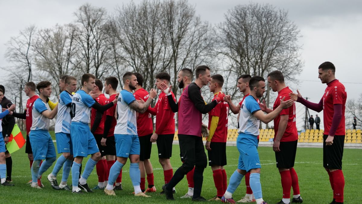 Football teams in red and blue kit shaking hands on a grassy pitch before the game. Football teams in red and blue kit shaking hands on a grassy pitch before the game.