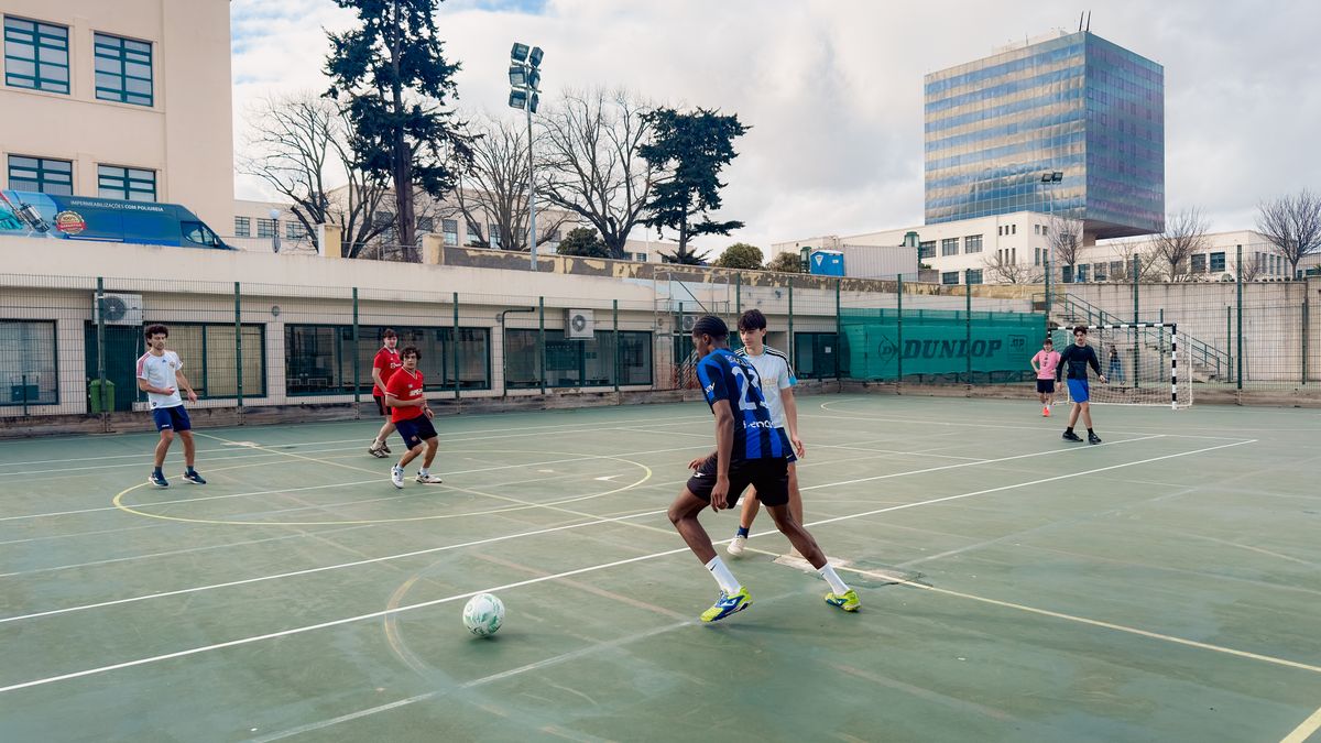 A group of teenagers playing soccer on an outdoor court in an urban environment, enjoying a sunny day.