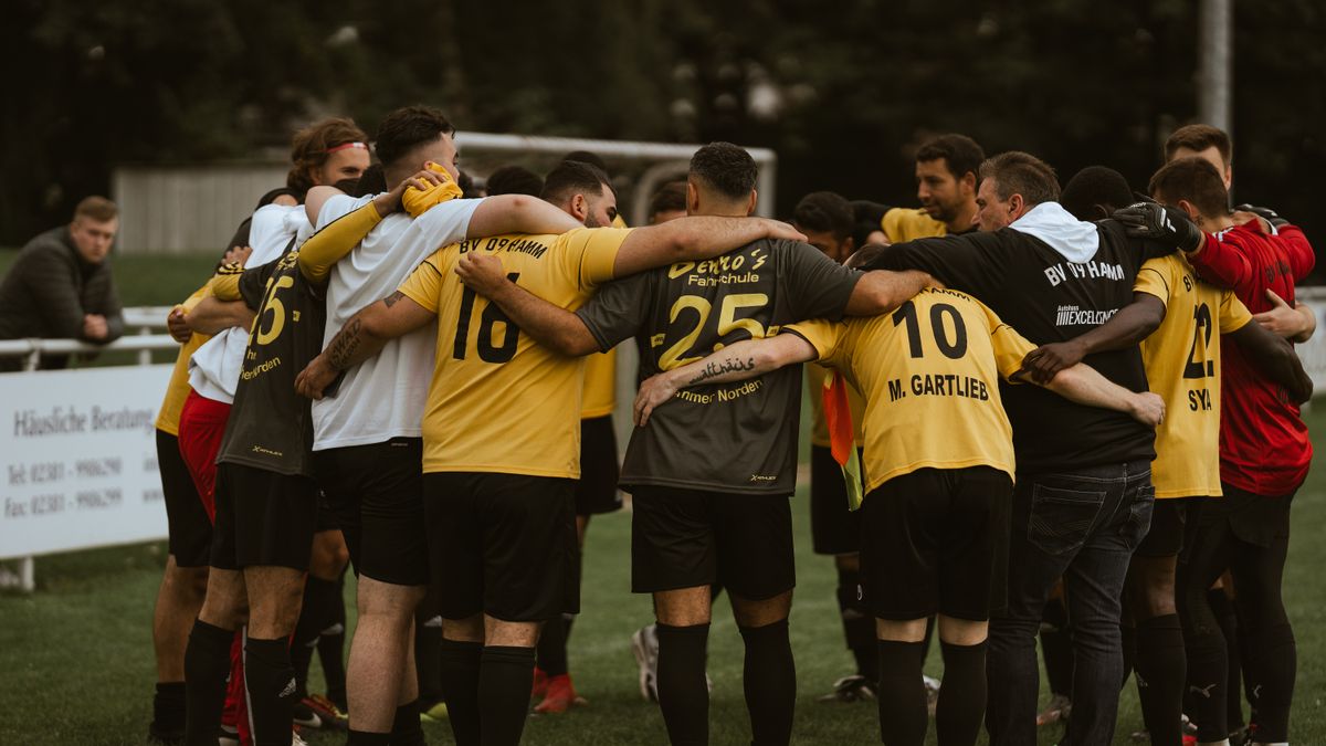 A soccer team in yellow and black jerseys huddles together on a grassy field, showing unity and teamwork.