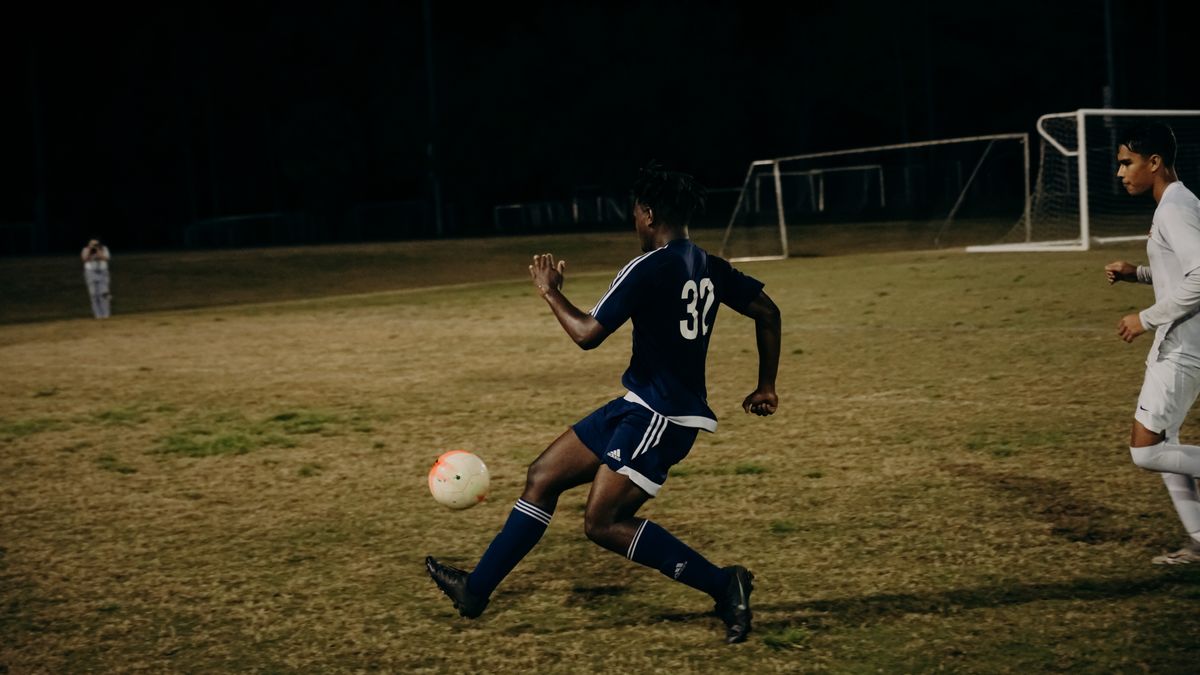 Two players compete fiercely during a nighttime football match on a grass field.