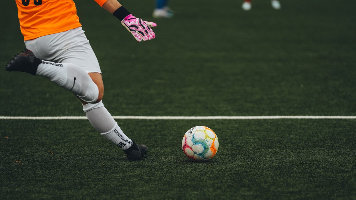A soccer goalkeeper prepares to kick a colorful ball on a grass field.
