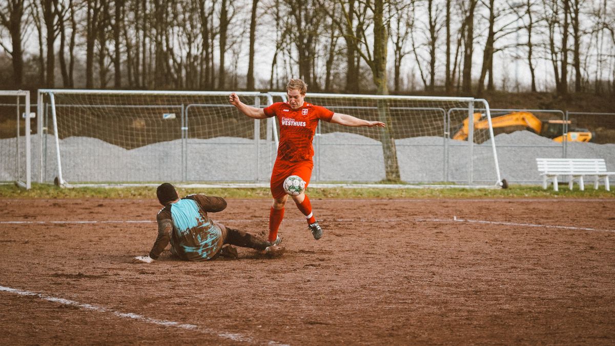 Two players compete fiercely in a soccer match on a muddy field.