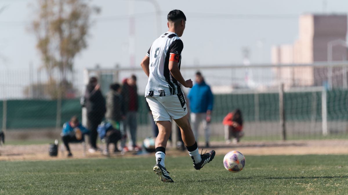 Young soccer player dribbles on field during a bright day match with spectators.