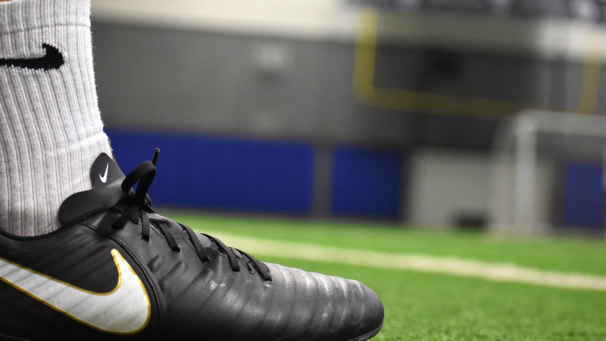 A detailed shot of a soccer cleat on an indoor turf field, emphasizing footwear and athletic activity.