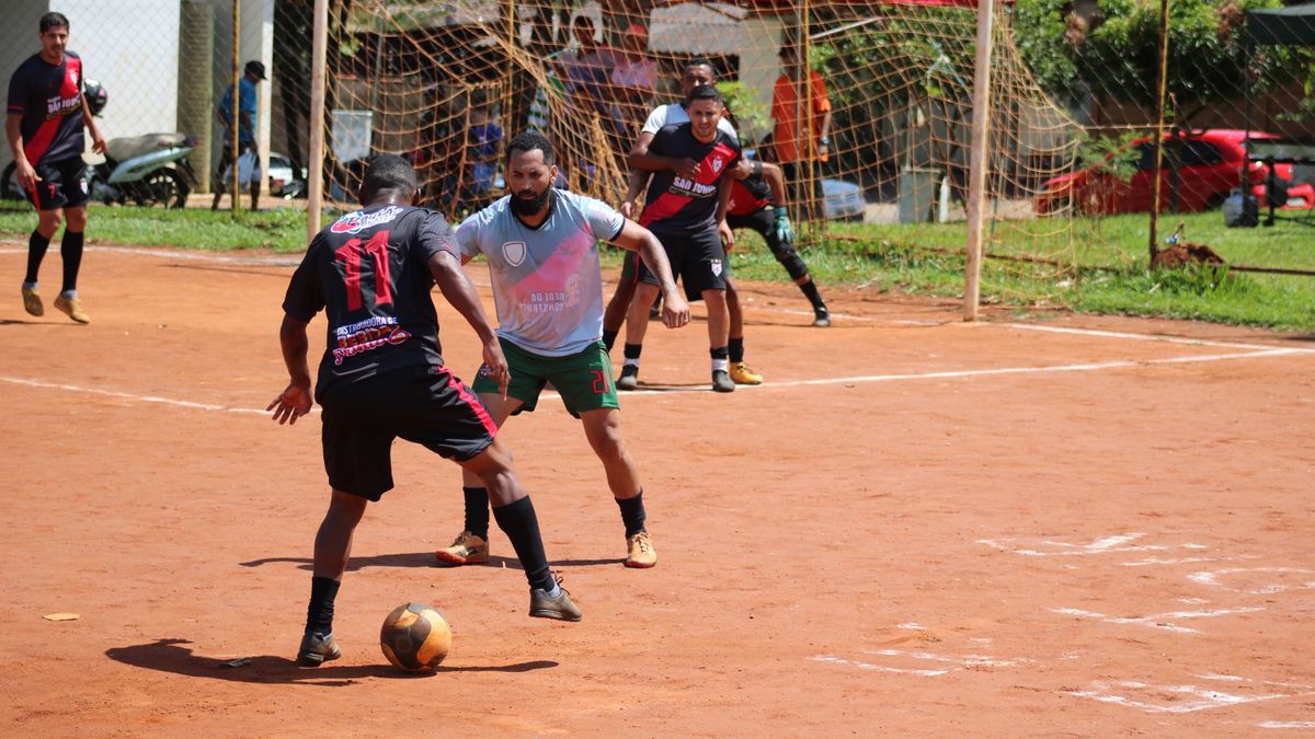 Men engaged in a competitive soccer game on a dirt field under a sunny sky.
