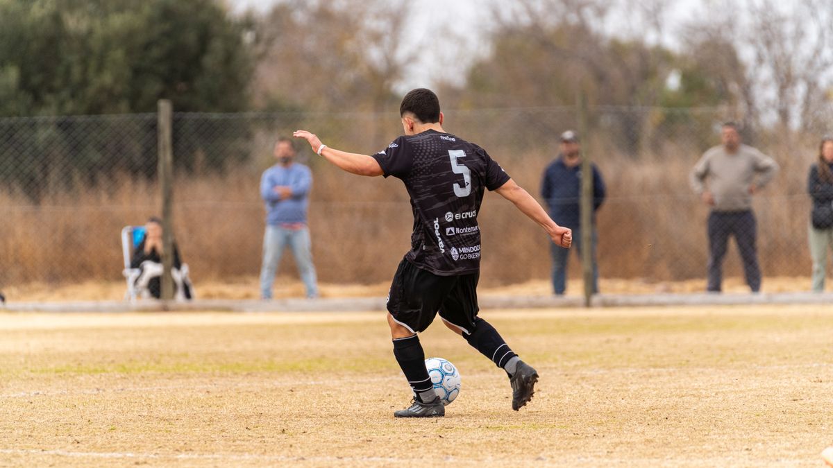 A soccer player wearing number 5 kicks a ball on an outdoor field.