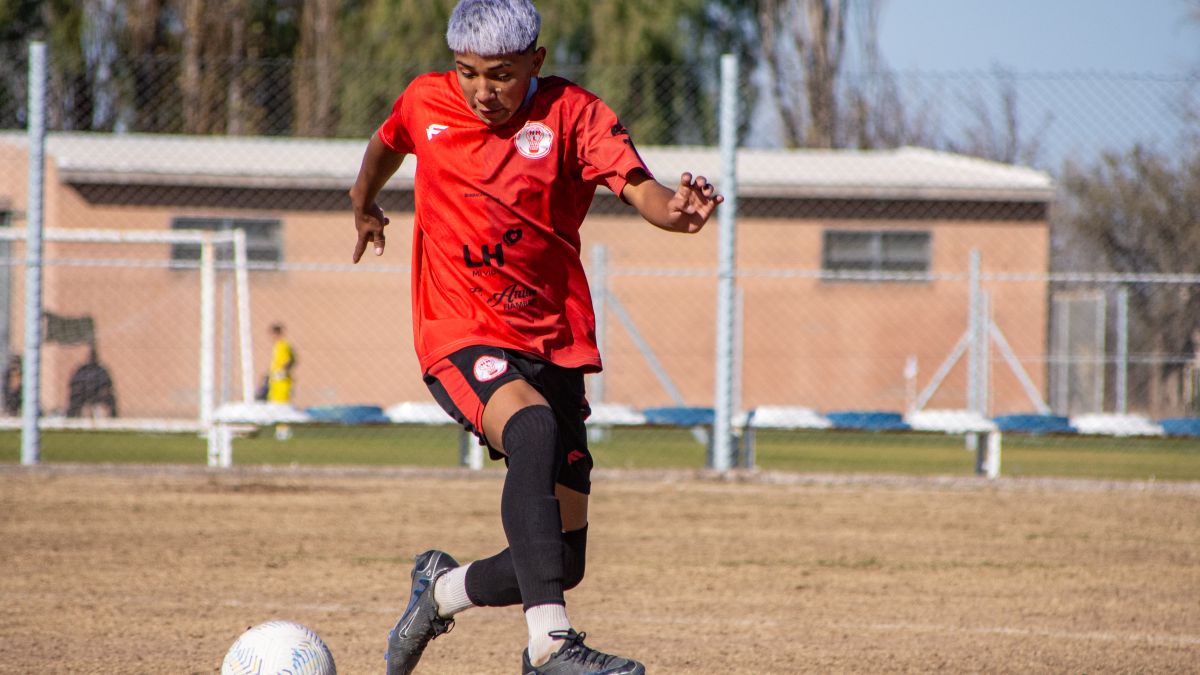 Young male soccer player skillfully dribbles the ball on a sunny day at an outdoor field.