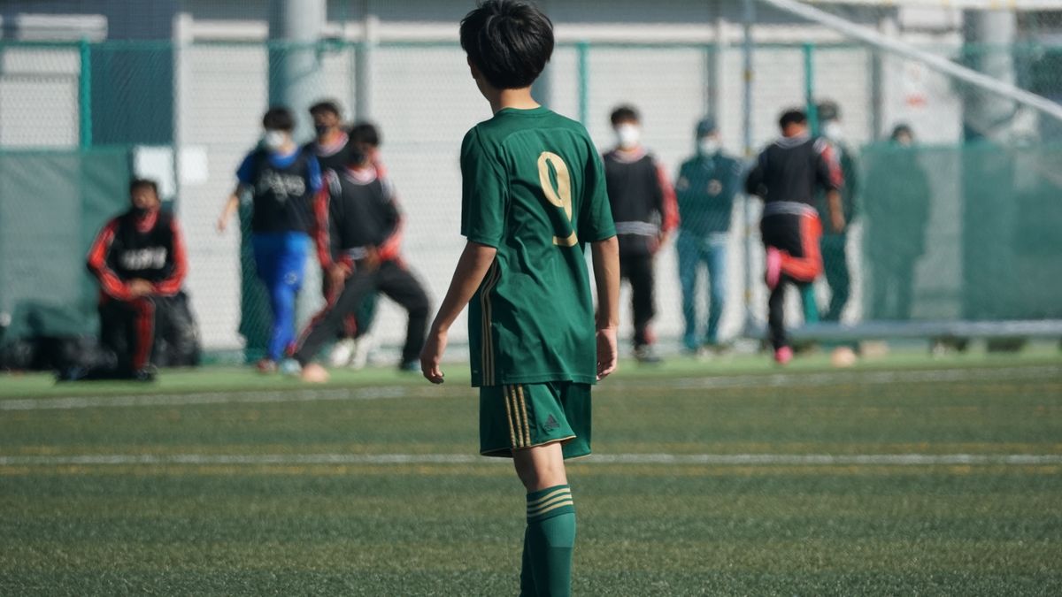 Youth soccer player in green jersey on football field during match.