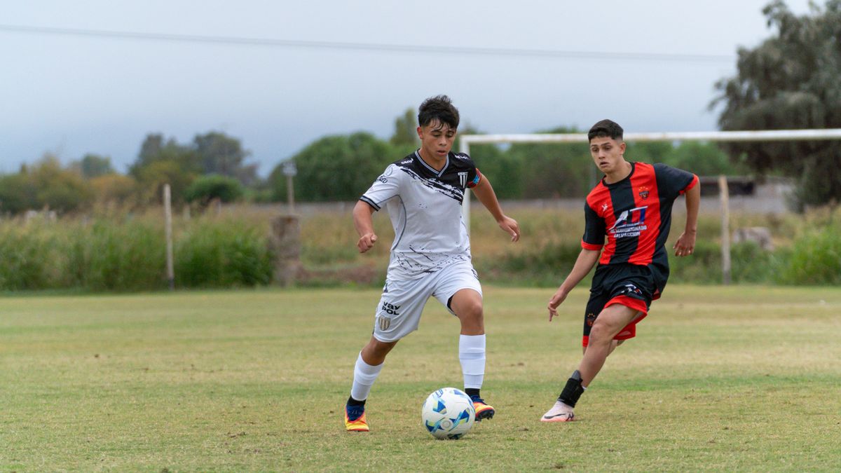 Two teenage soccer players in uniforms compete on an outdoor field. Two teenage soccer players in uniforms compete on an outdoor field.