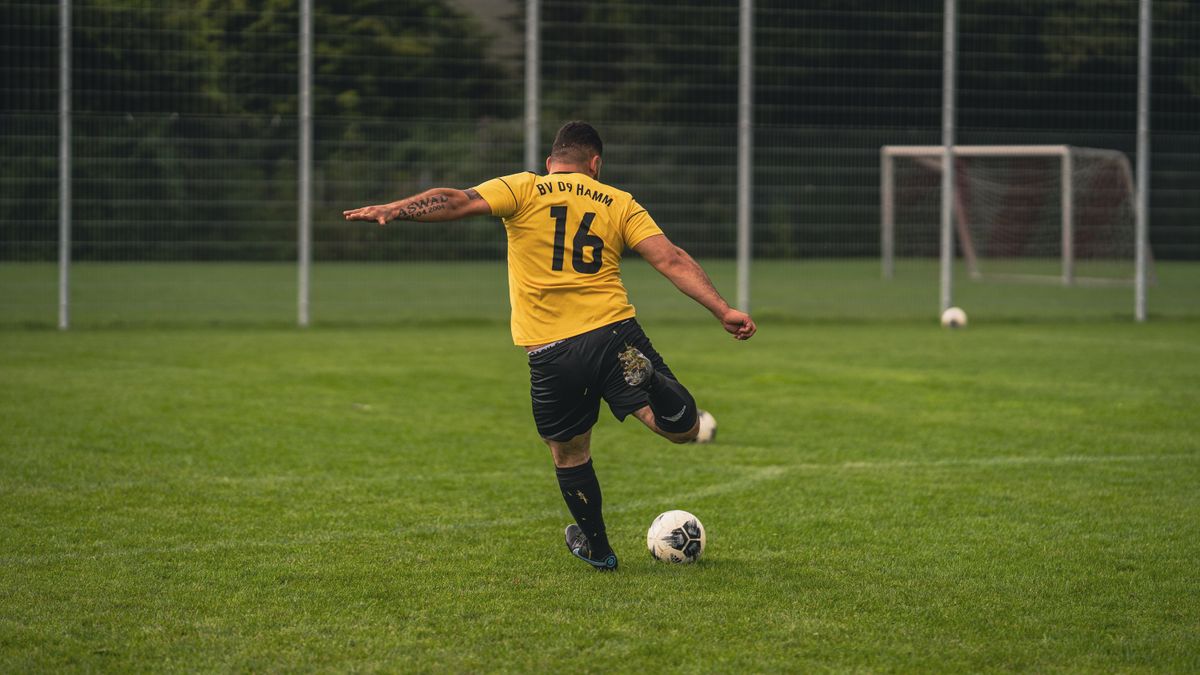 Back view of a football player in yellow jersey kicking a ball on a grass field. Back view of a football player in yellow jersey kicking a ball on a grass field.