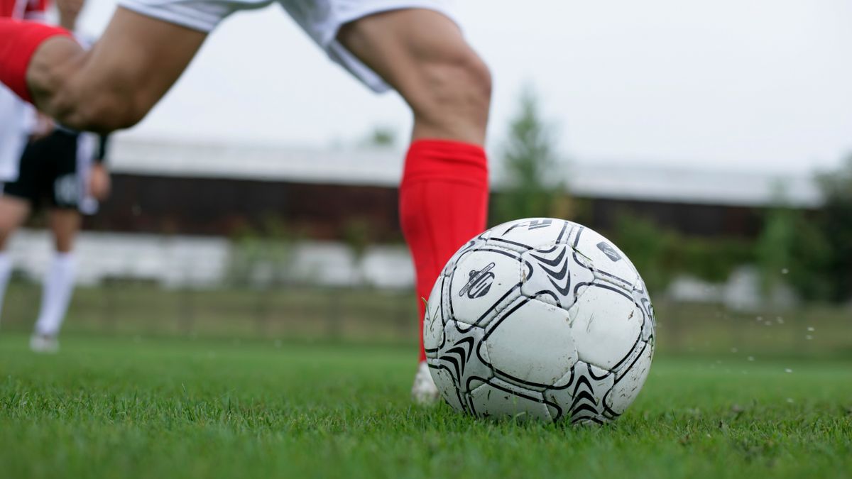 Close-up of a soccer player kicking a ball during a daytime match. Close-up of a soccer player kicking a ball during a daytime match.