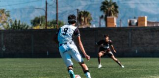 Dynamic image of two soccer players in action on the field under a clear sky.