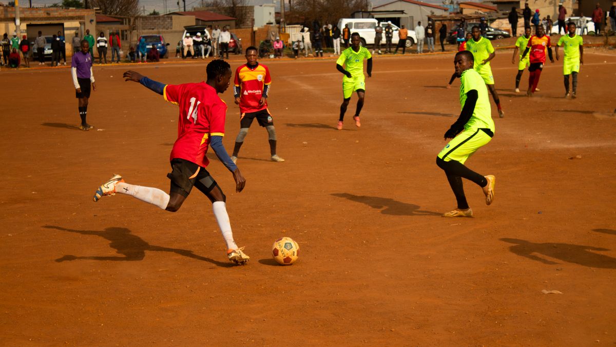 Local football match on a dusty field with players in colorful jerseys engaged in action.