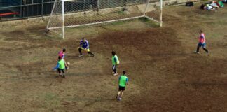 Players engaged in a soccer match on a muddy field, viewed from above.