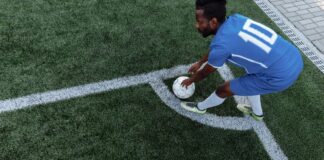 A soccer player in a blue jersey prepares to kick the ball from the corner on an artificial turf field.