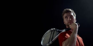 A thoughtful male tennis player holding a racket, set against a dark background.