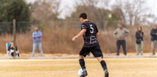 Amateur soccer player with number 5 jersey in action during a match on a natural grass field.