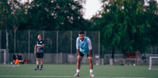 Male soccer player in uniform standing in field and leaning on hands during training in grassy field