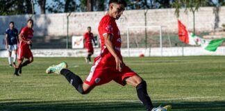 Soccer player in red uniform powerfully kicking ball during a daytime match.