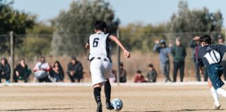 Young soccer players in action on a sunny outdoor field with spectators.