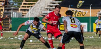 Action-packed soccer game between teams in red and black uniforms on a sunny outdoor field.