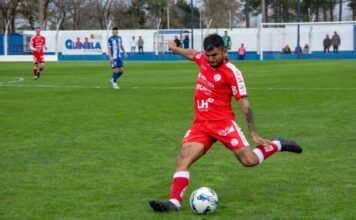 Soccer player in red jersey kicks ball during intense outdoor match.