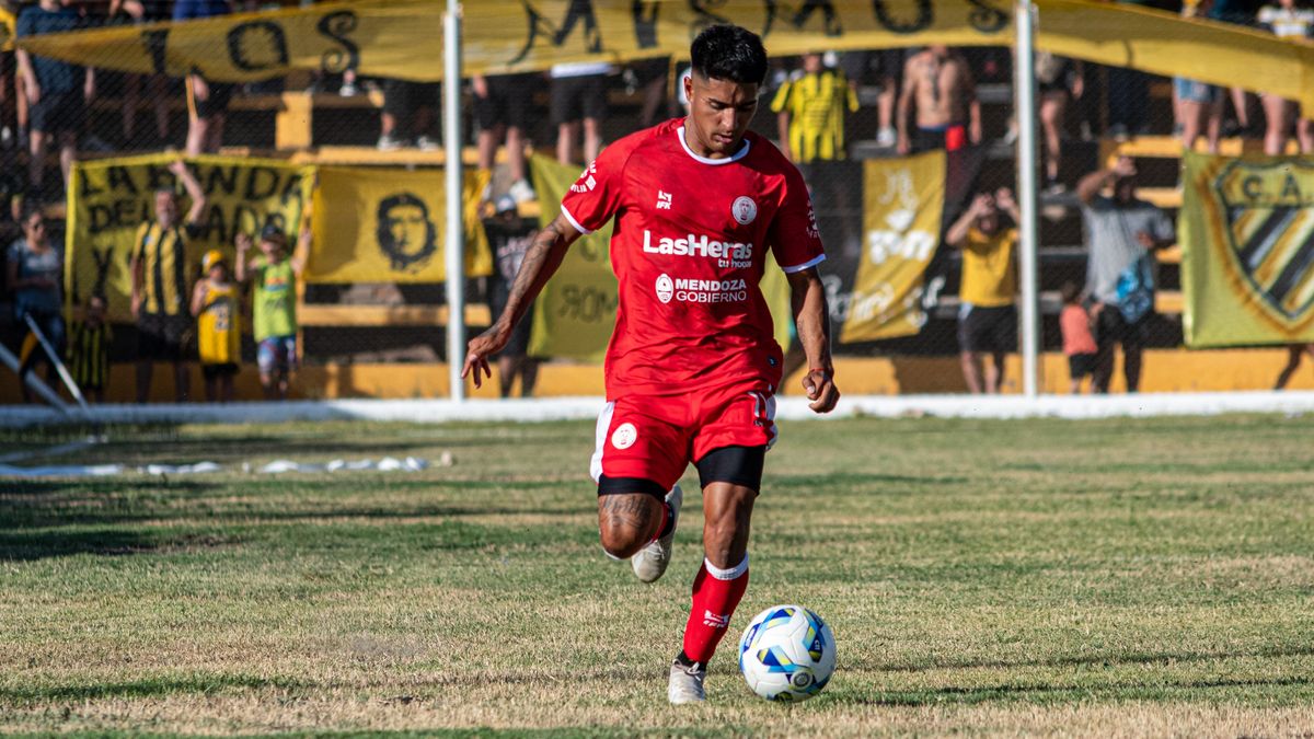 A soccer player in red uniform dribbling during a daytime match with spectators. A soccer player in red uniform dribbling during a daytime match with spectators.