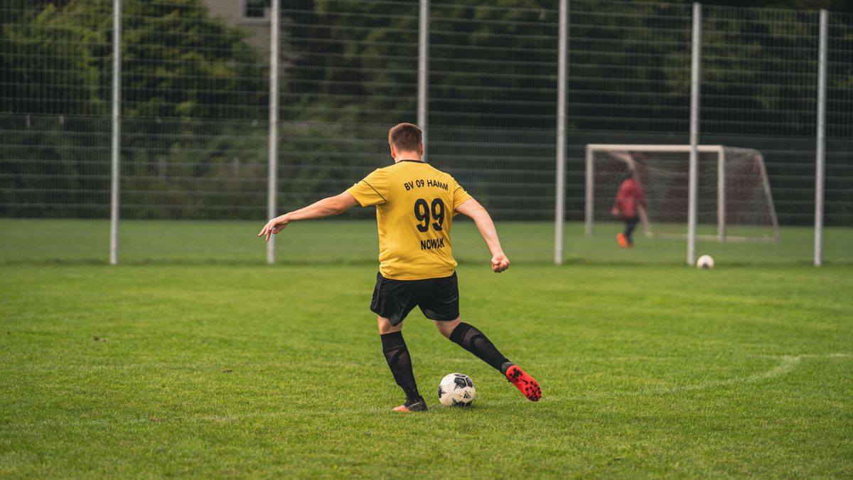 A soccer player in a yellow jersey kicking a ball on a lush green field during the day. A soccer player in a yellow jersey kicking a ball on a lush green field during the day.