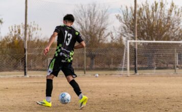 Teen soccer player wearing number 13 practicing on an outdoor field.