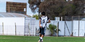 A teenage soccer player wearing number six dribbles the ball outdoors in a park.