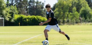 A teenager playing soccer on a sunny day, dribbling the ball on a grassy field.