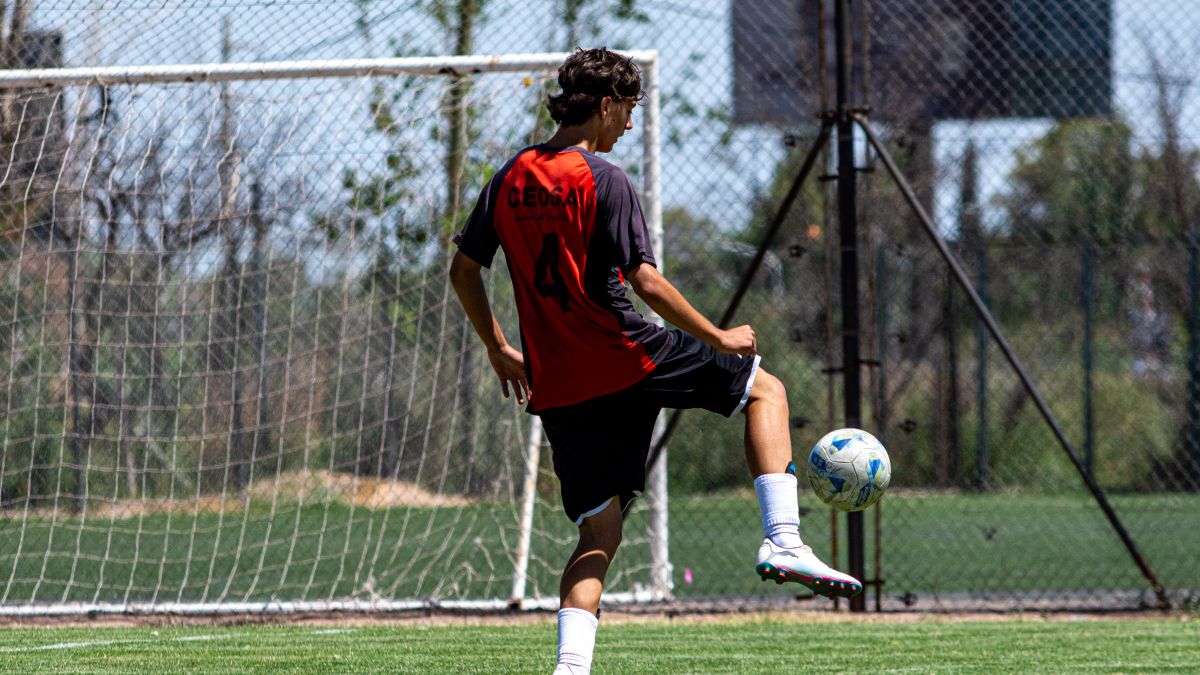 Teenager in red jersey playing soccer on an outdoor field during daytime. Teenager in red jersey playing soccer on an outdoor field during daytime.