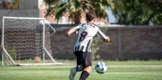 A soccer player in action, wearing a striped jersey, kicking a ball towards the goal during a sunny day match.