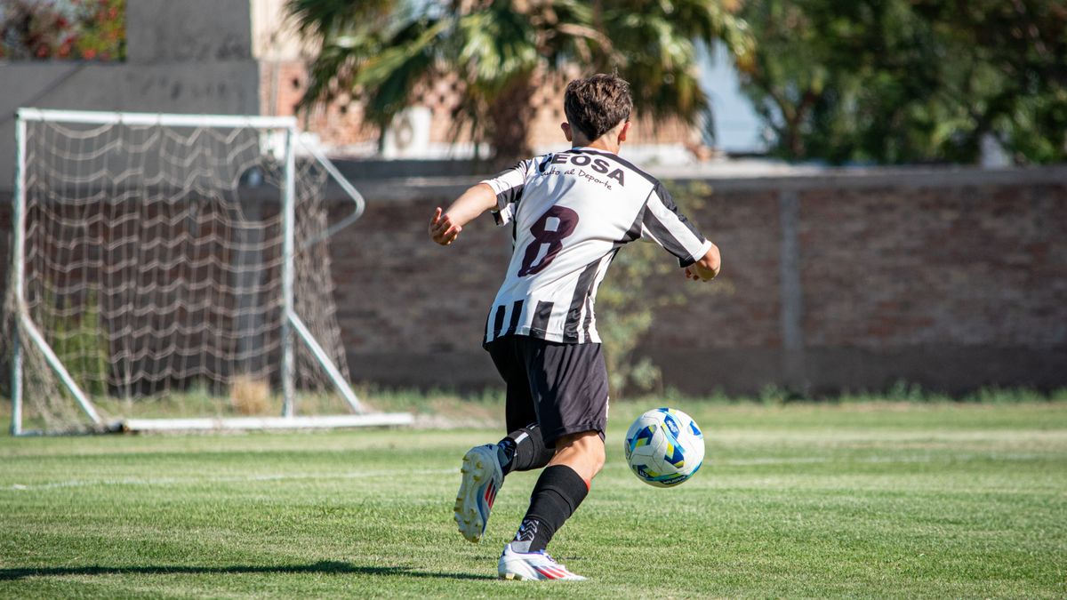A soccer player in action, wearing a striped jersey, kicking a ball towards the goal during a sunny day match. A soccer player in action, wearing a striped jersey, kicking a ball towards the goal during a sunny day match.