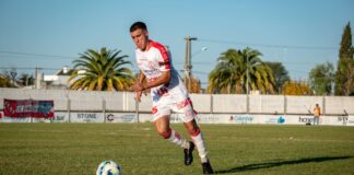 A soccer player in sportswear dribbles the ball on an outdoor field during a daytime match.