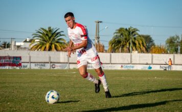 A soccer player in sportswear dribbles the ball on an outdoor field during a daytime match.