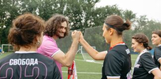 Soccer team celebrating victory on field with coach, exchanging fist bumps and medals.