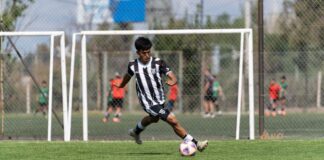Teen soccer player kicking a ball during a daytime match, showcasing athletic skills on the field.