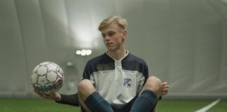 Teen soccer player sitting on indoor field, holding ball in training facility.