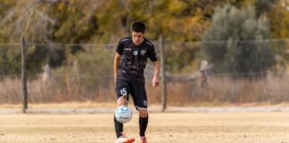 Teen soccer player wearing black jersey practices ball control on an outdoor field in autumn.