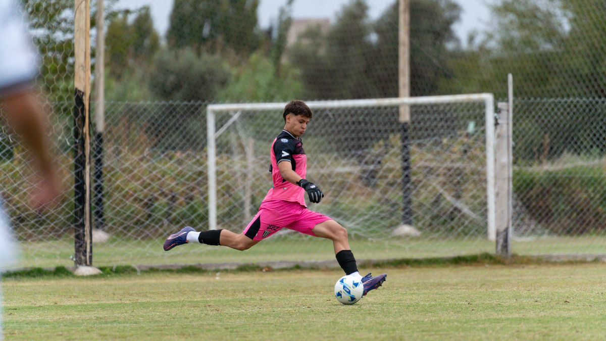 A young goalkeeper in pink uniform kicks a soccer ball on an outdoor field. A young goalkeeper in pink uniform kicks a soccer ball on an outdoor field.