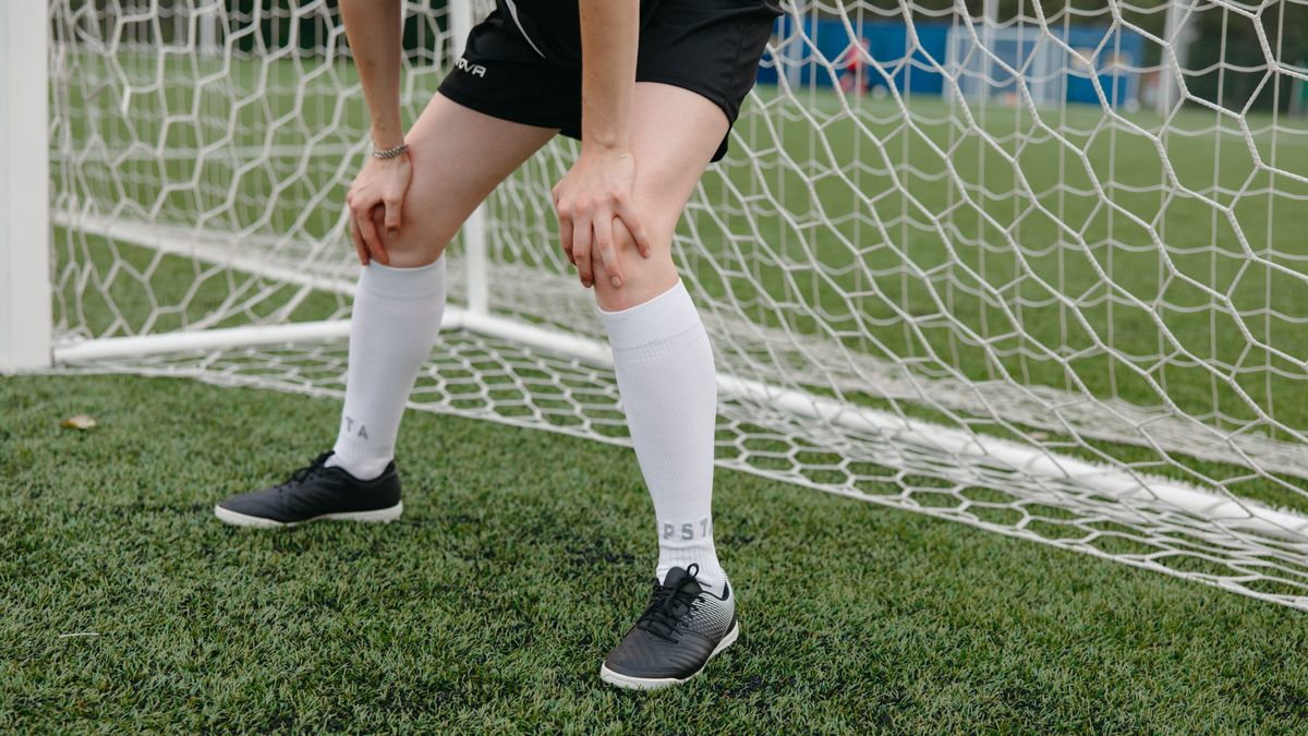 Soccer player resting in front of the goal on a grassy field, wearing sports uniform and sneakers. Soccer player resting in front of the goal on a grassy field, wearing sports uniform and sneakers.