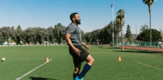 A soccer player warming up with exercises on a sunny day at an outdoor field.