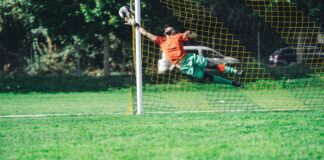 Goalkeeper leaping to save a soccer ball during an outdoor match.
