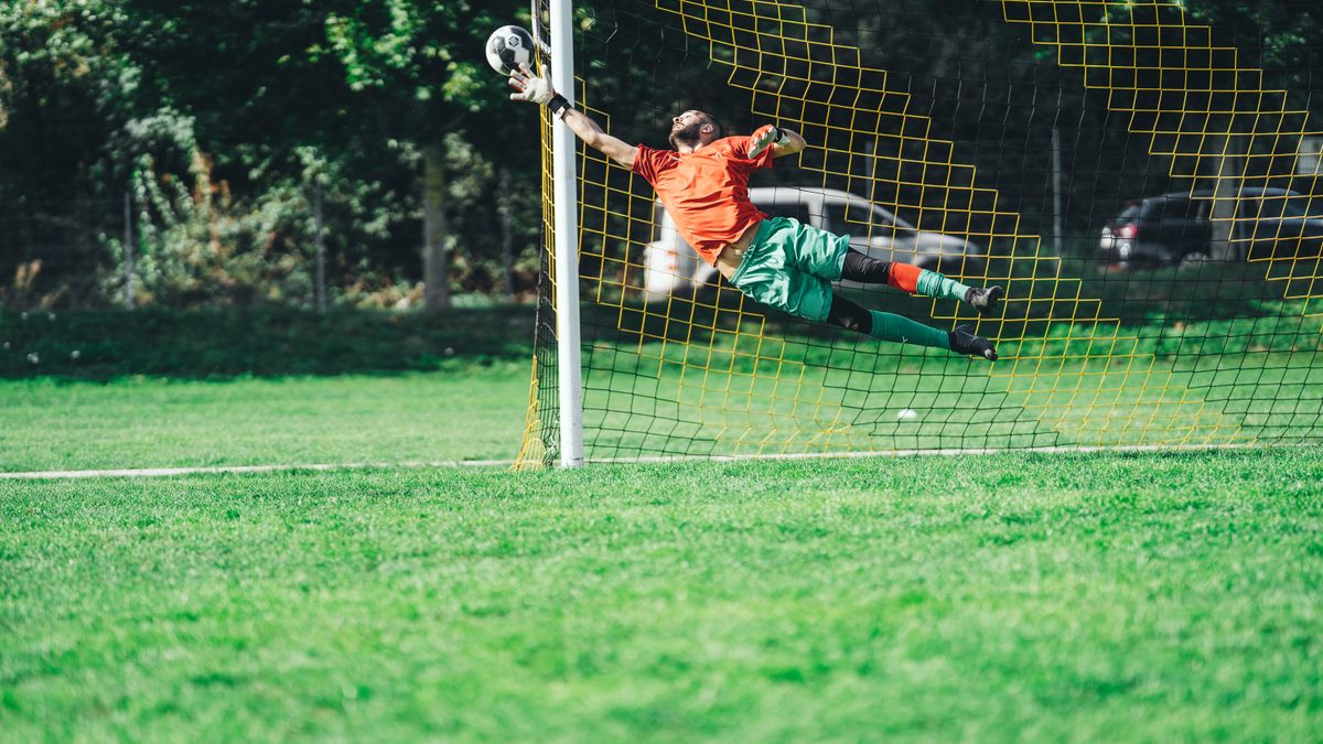 Goalkeeper leaping to save a soccer ball during an outdoor match. Goalkeeper leaping to save a soccer ball during an outdoor match.